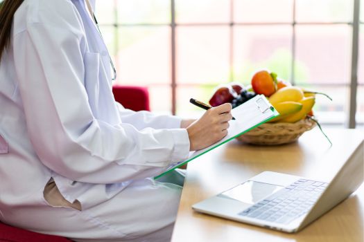 Weight loss specialist taking notes. Bowl of fruit. Labtop on the table